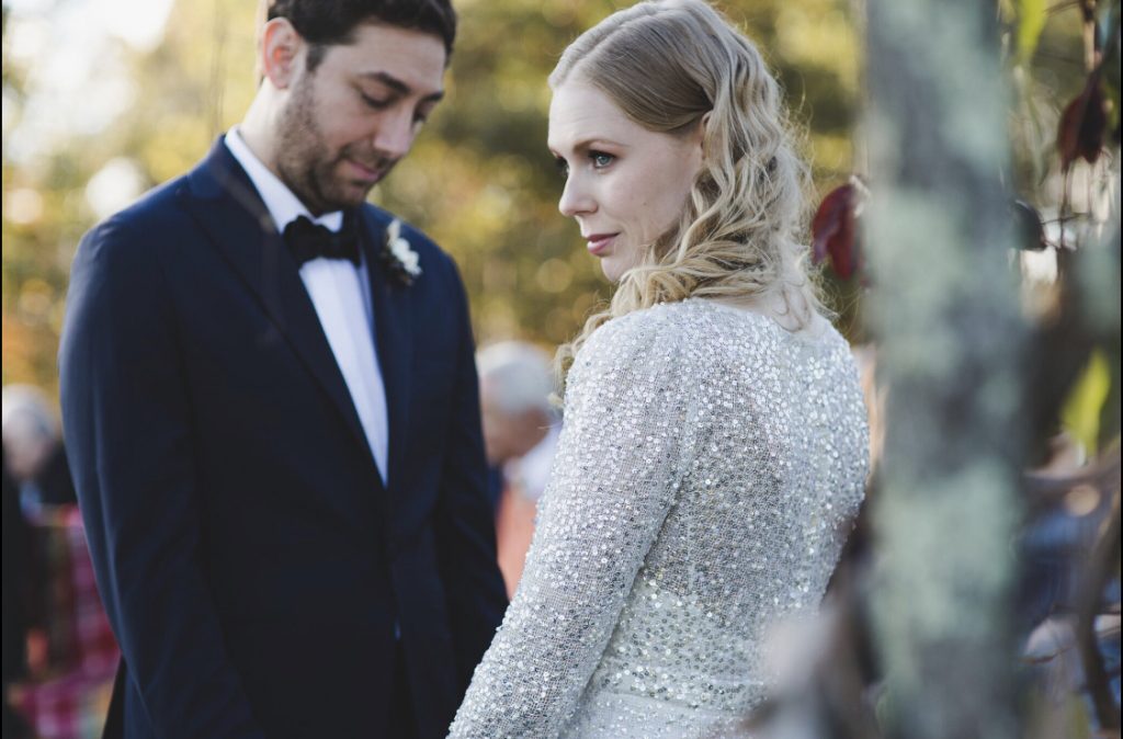 Groom on the left, black and white in tuxedo, blonde waves on the bride with spangled dress. In the woods.