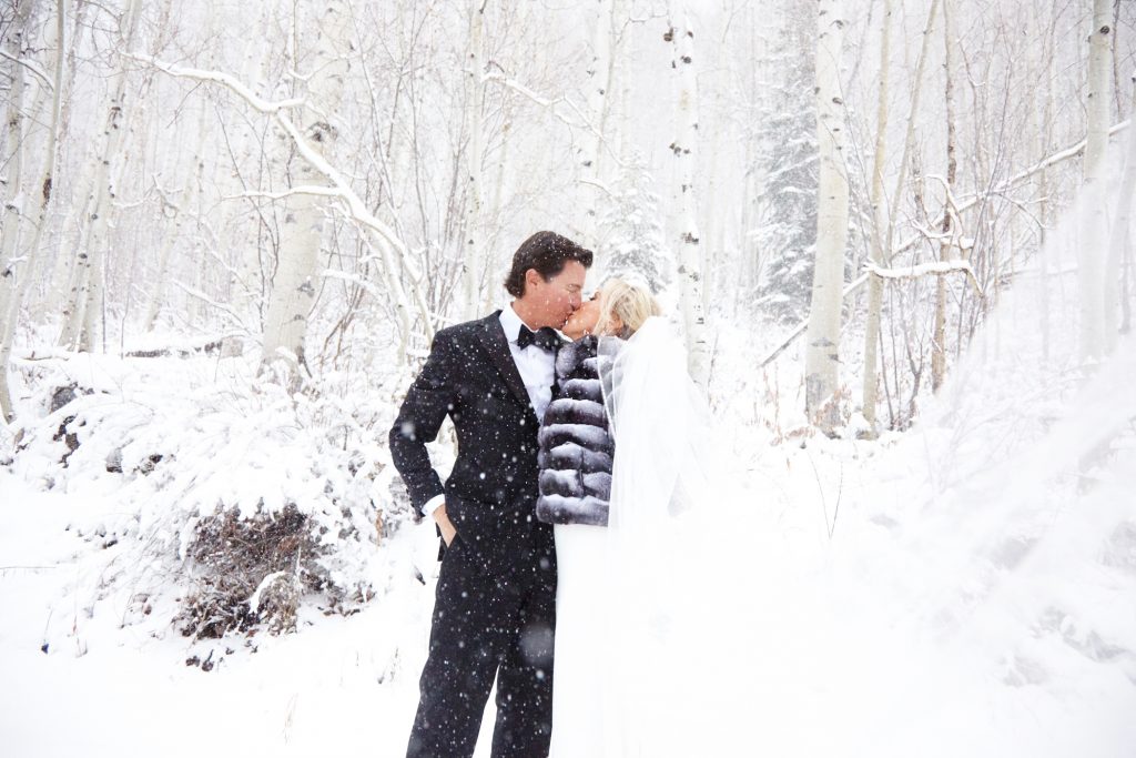 Bride and groom kissing in a winter wonderland - snowy background and trees