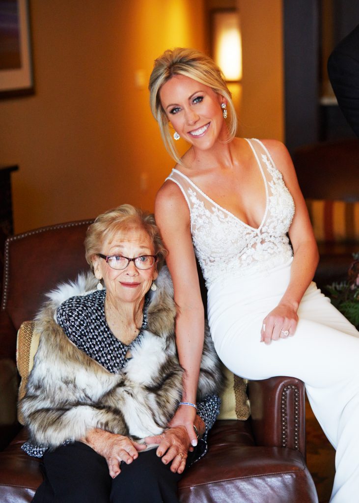 Bridal portrait, blonde bride in white lacy gown with lace inset in bodice. Gram next to her with glasses, red lipstick and a fur stole.