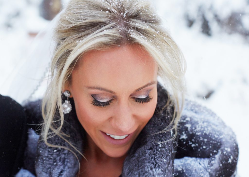 Closeup shot from above, bride looking down with a dusting of snow in her hair, silver eyeshadow and long lashes visible. 