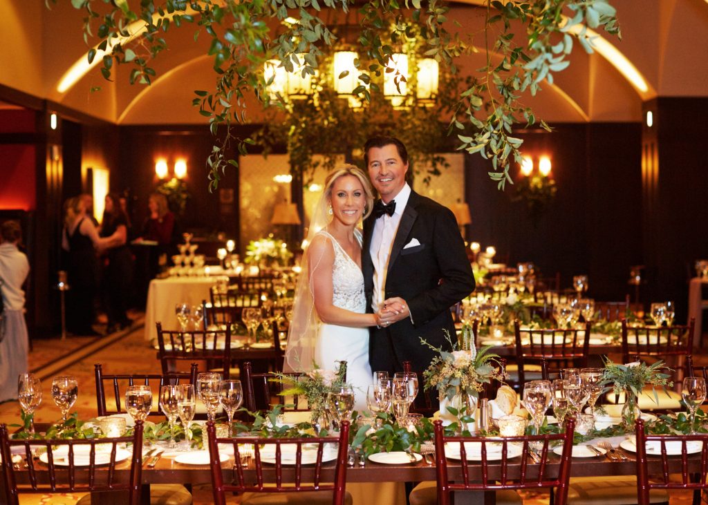 Bride and groom in banquet hall, warm lighting and green centerpieces