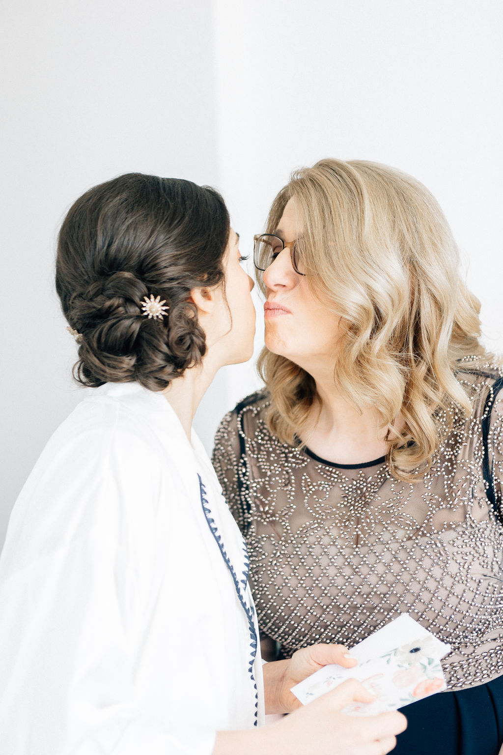 Bride with dark, shiny hair swept into low textured bun with sparkling hair pin kisses her mom on wedding day, William Vale Hotel
