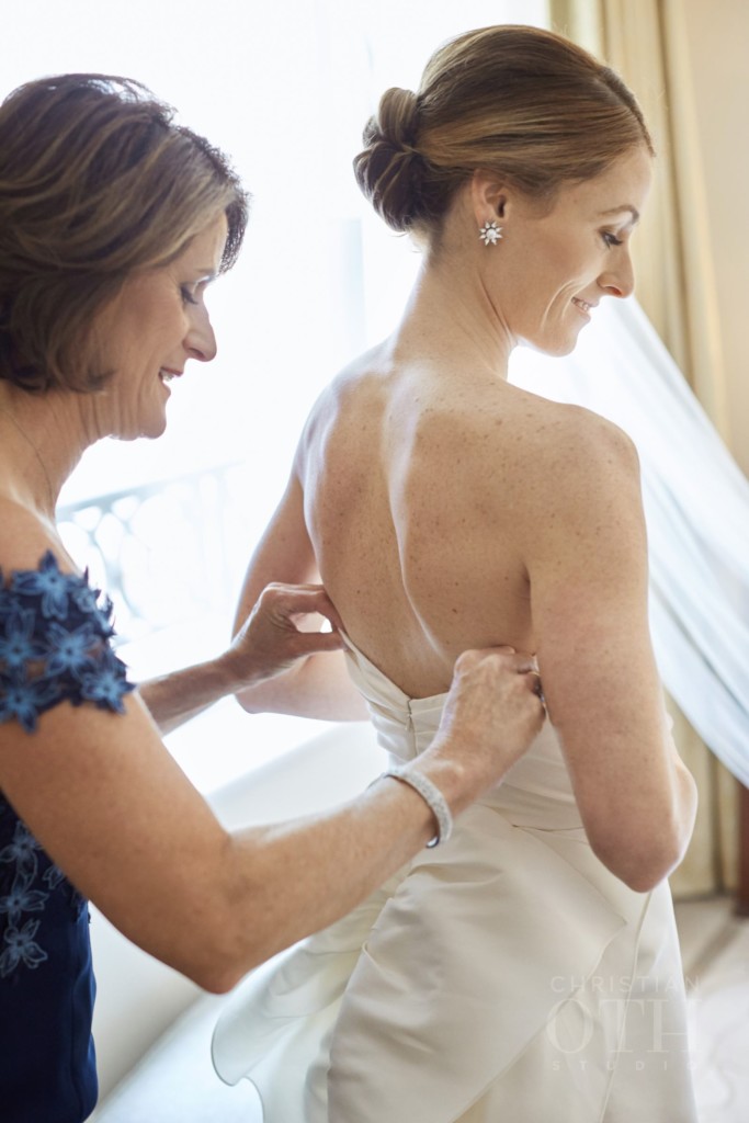 Mother of the bride adjusts dress on bride with modern, chic chignon, before wedding at Peninsula Hotel in New York City