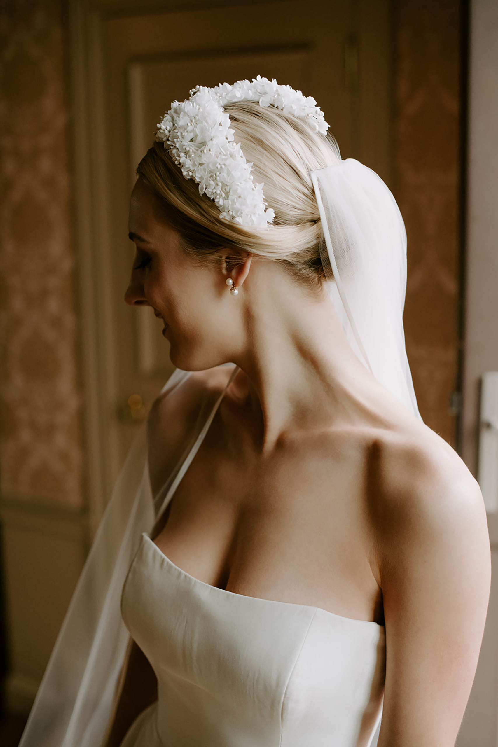 Blonde bride with classic strapless dress and elaborate flowered headband over her simple chignon, photographed at Oheka Castle