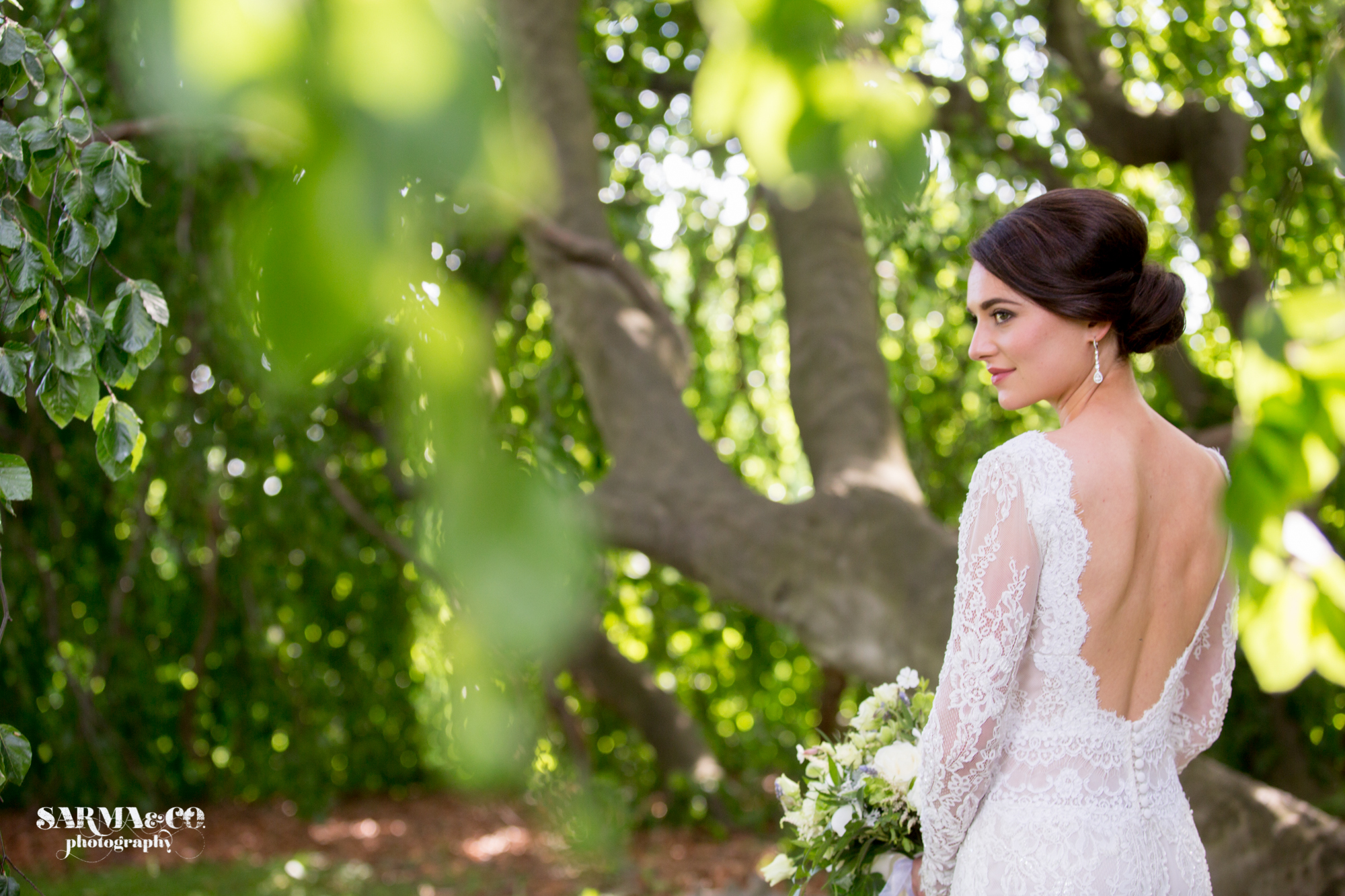 Brunette bride with backless dress, smokey eyes, and contoured cheeks poses in her backless dress for her spring wedding at the Lindhurst Castle in Tarrytown, New York
